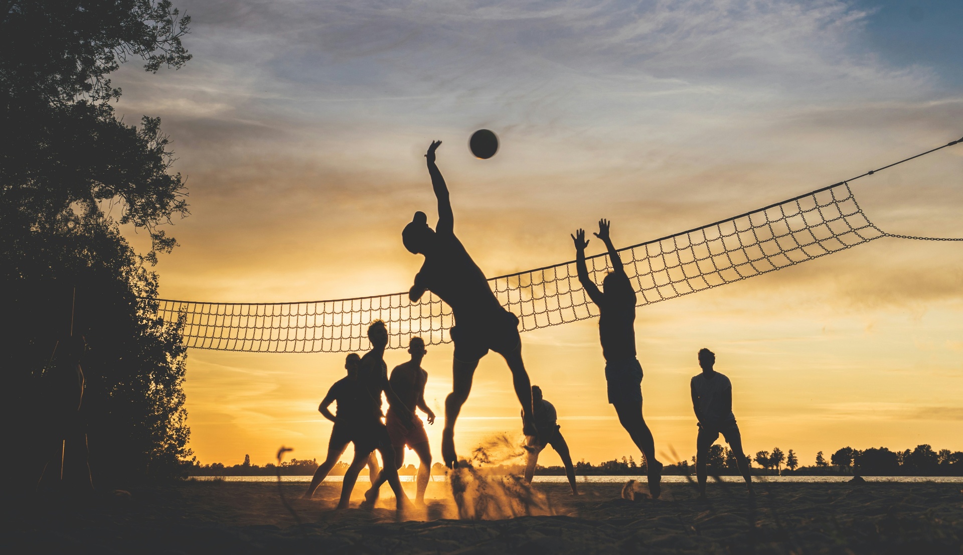 Beach volleyball players silhouetted against a sunset sky