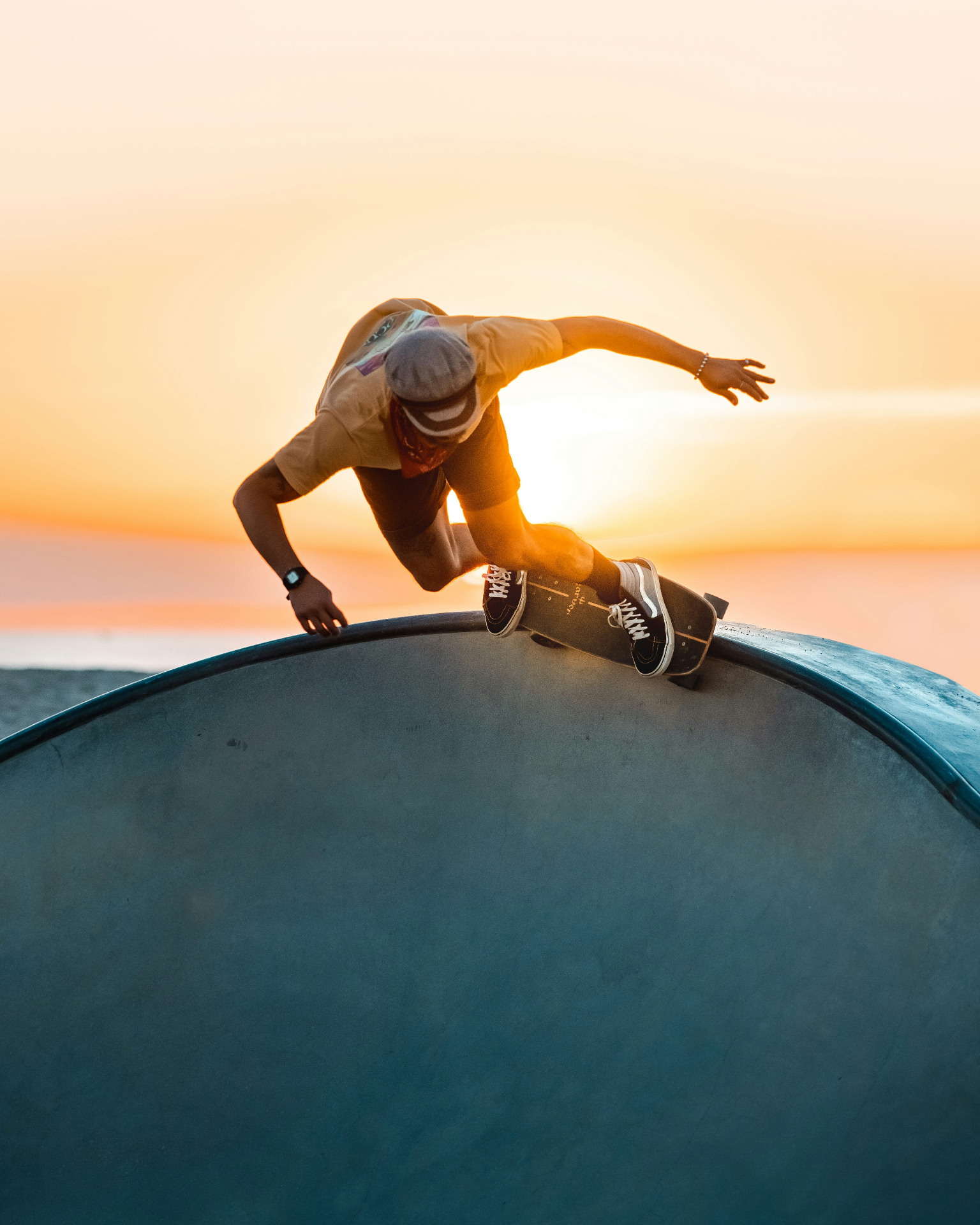 Skateboarder dropping into a bowl at sunset
